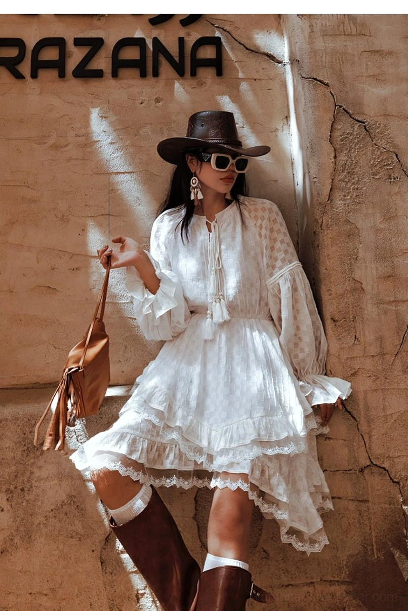 Side view of a white western ruffle midi dress with voluminous sleeves ruffled cuffs and brown knee high boots against a stone wall