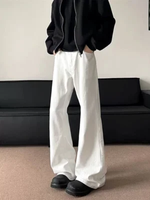 Rear left side view of white wide-leg flared jeans styled with a black zip-up streetwear jacket in an indoor studio
