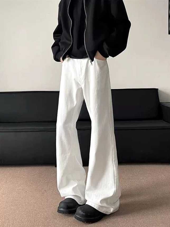 Rear left side view of white wide-leg flared jeans styled with a black zip-up streetwear jacket in an indoor studio