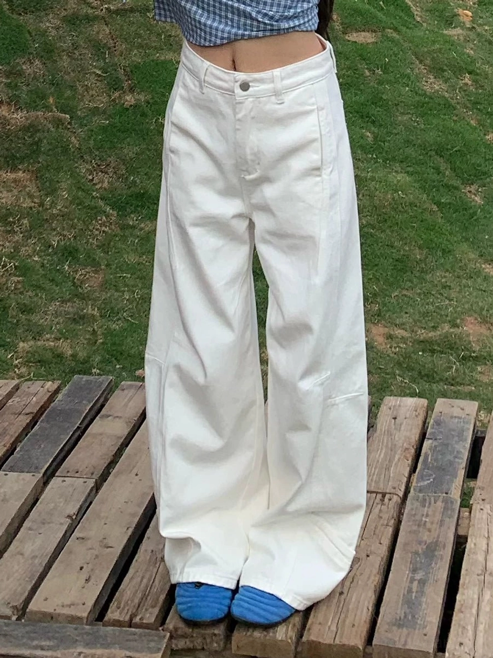 Close-up of white wide-leg jeans with curved vertical panel seams, front pockets, natural-rise waist, and structured cotton denim