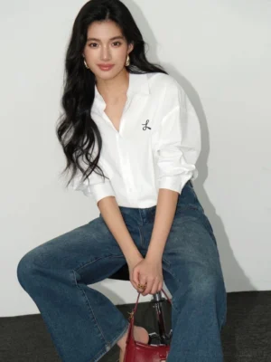 White women's embroidered button-down streetwear shirt shown in a relaxed sitting outfit with wide-leg blue jeans and red handbag