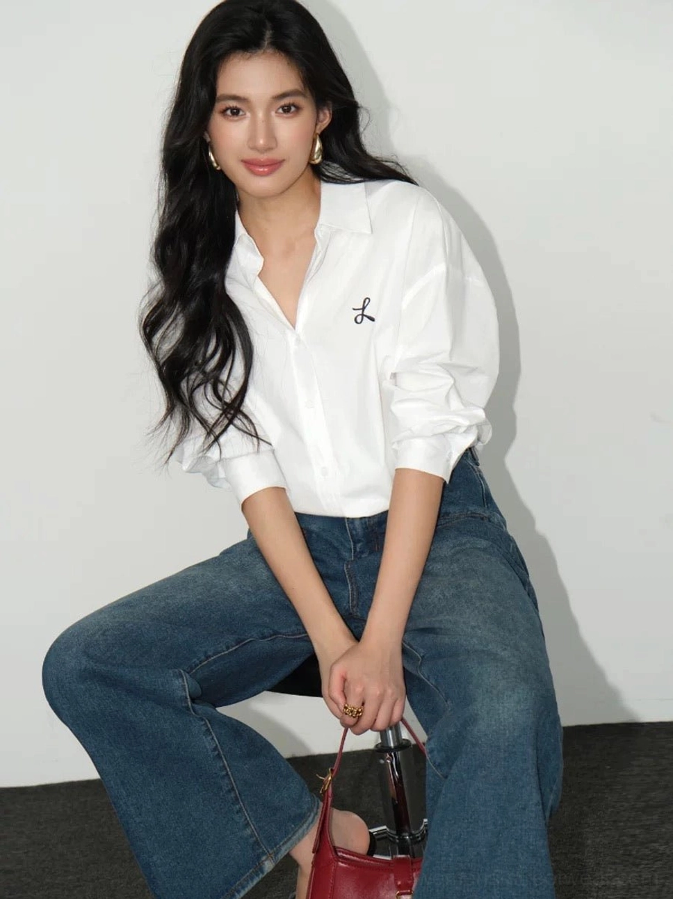 White women's embroidered button-down streetwear shirt shown in a relaxed sitting outfit with wide-leg blue jeans and red handbag