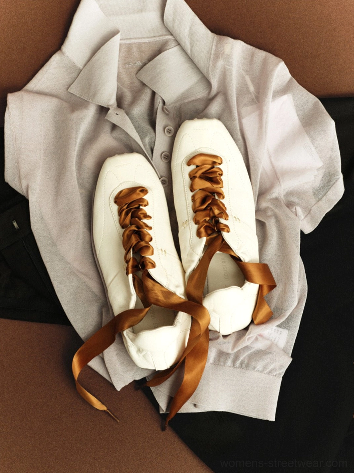 White women's retro trainers with brown ribbon laces styled beside a light grey button-up shirt in a fashion flat lay