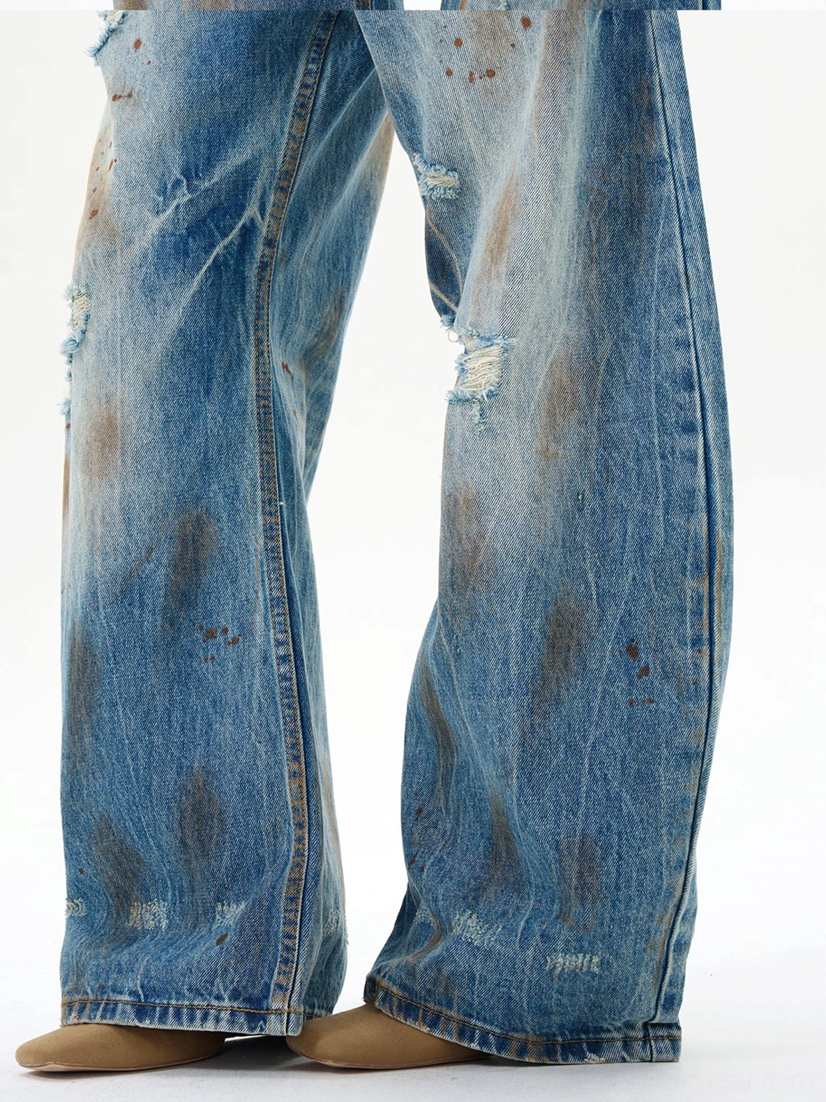 Lower leg detail of vintage washed blue wide-leg jeans with ripped distressing, textured denim, and styling with ankle boots