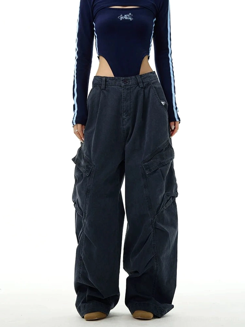 Wide-leg streetwear cargo workwear pants styled on a female model with a cropped top, showing the relaxed high-waisted silhouette, front pleats, and oversized utility pockets