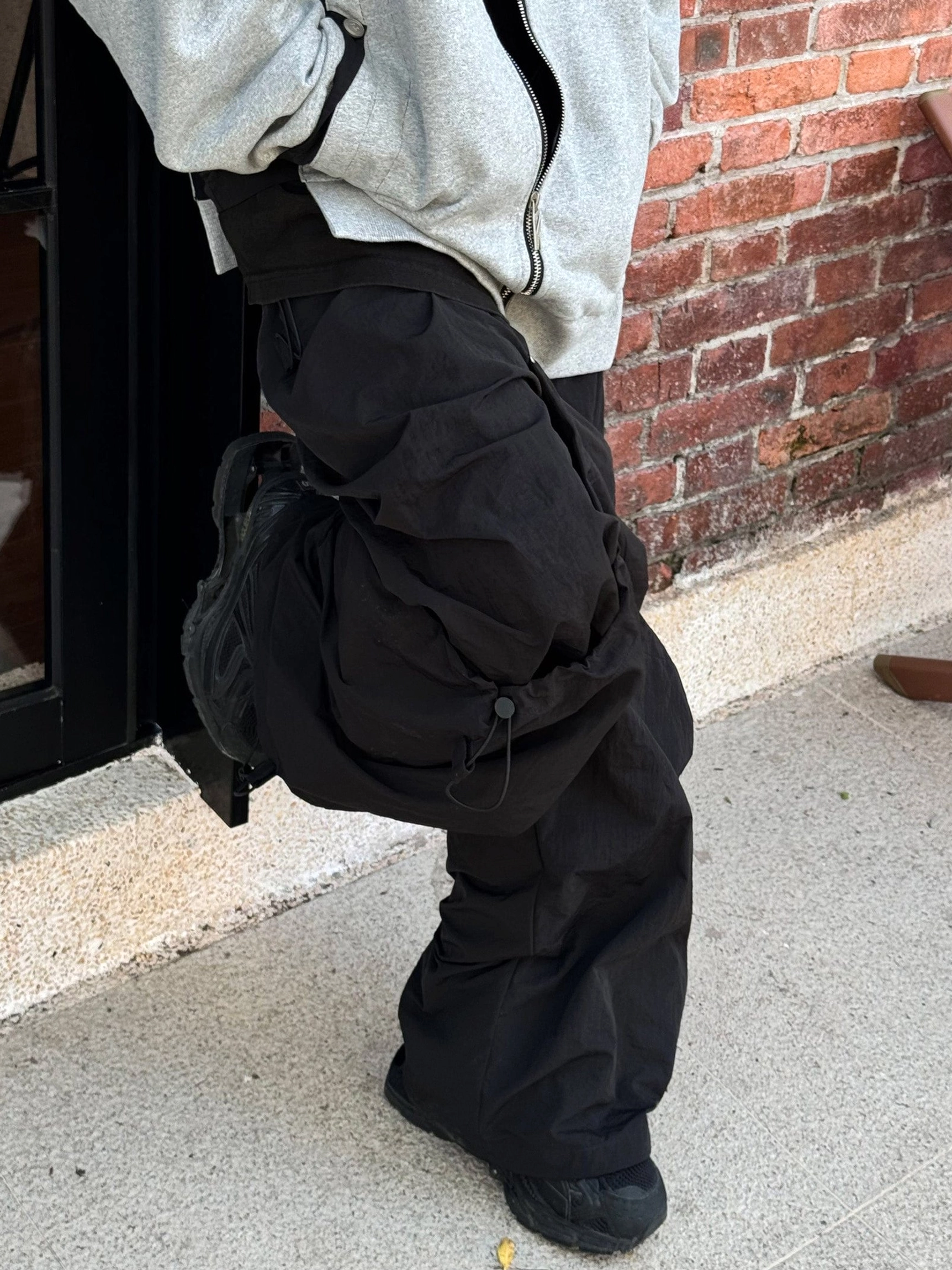 Streetwear outfit featuring wide leg technical cargo pants styled with a grey zip up jacket and crossbody bag outdoors
