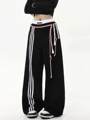 Black wide-leg varsity stripe track pants with contrast drawcords styled with cropped black top and sneakers front view