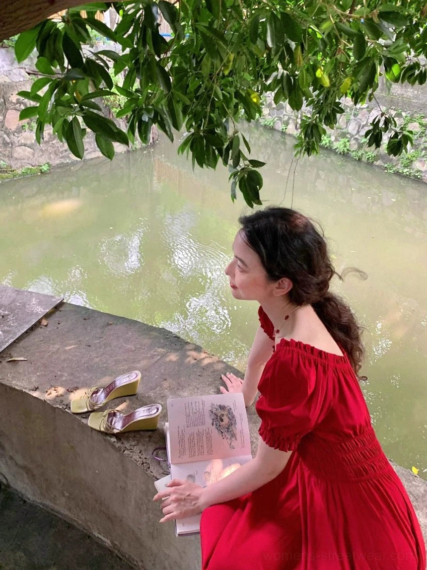 Wine red puff sleeve smocked waist mini dress shown from the rear side with a relaxed romantic silhouette in a rural riverside setting