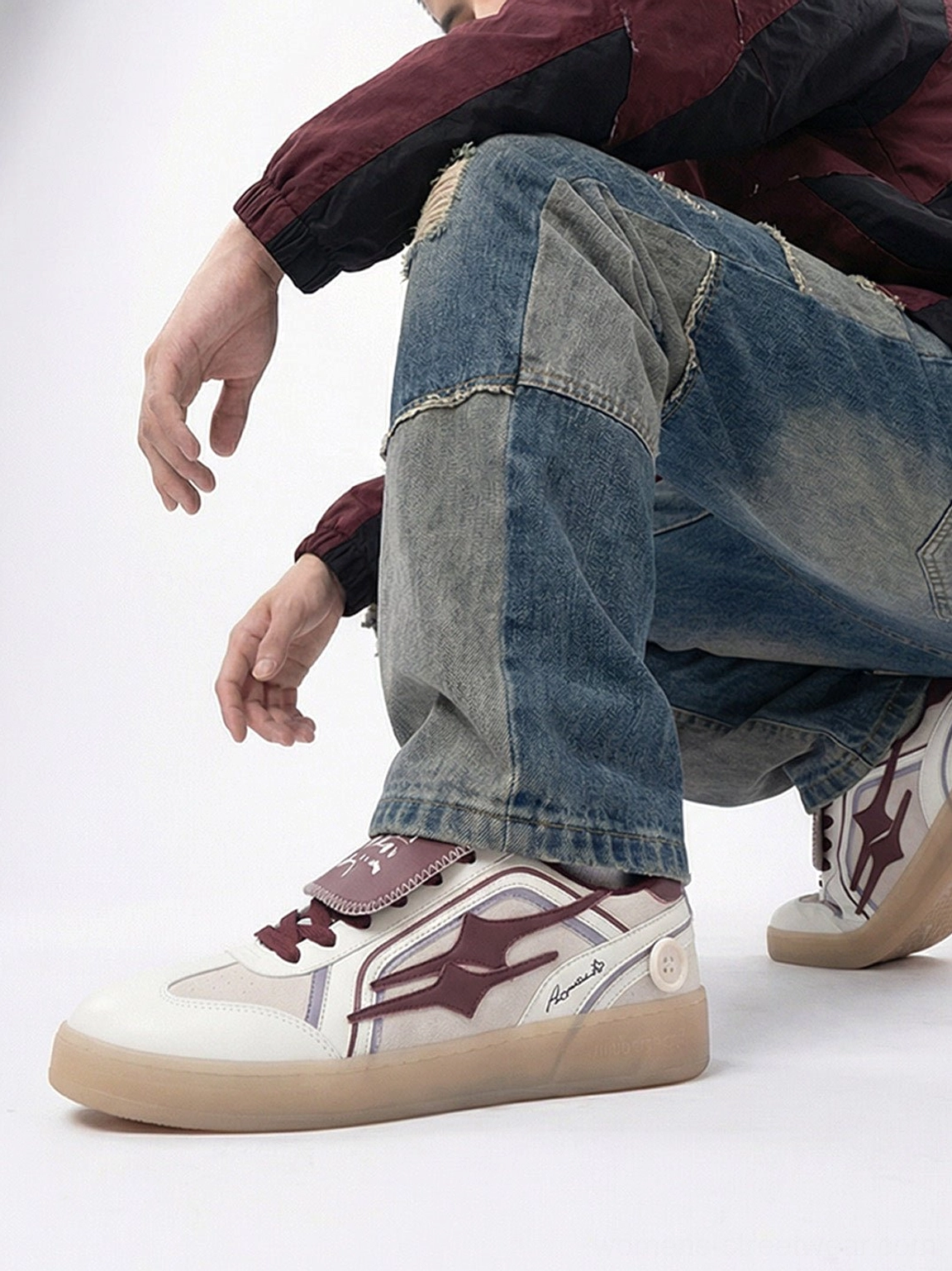 Close low-angle view of wine red retro sneakers with tongue strap and side emblem styled with distressed jeans