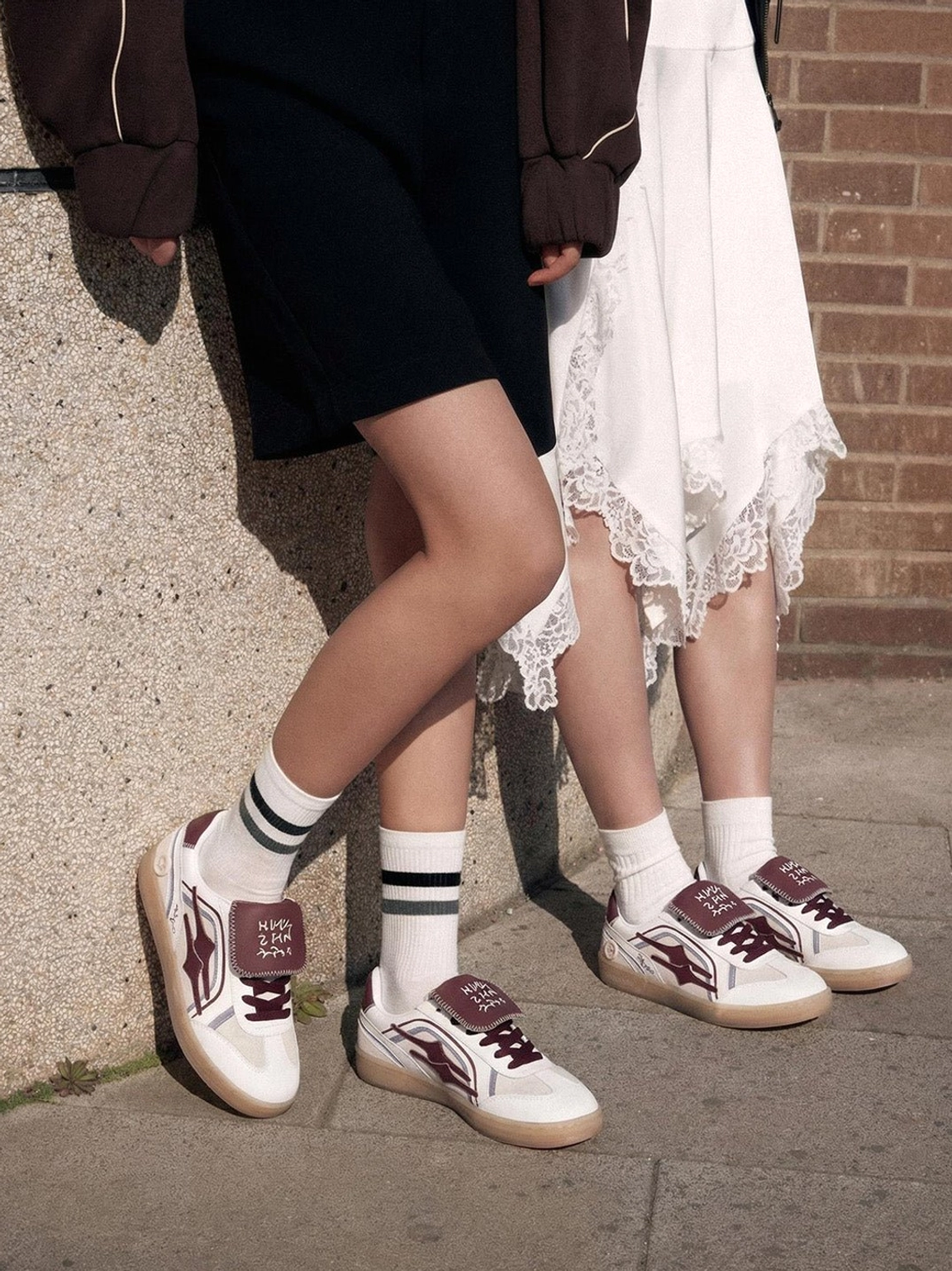 Two models wearing wine red strap retro sneakers with white socks in an outdoor urban streetwear setting