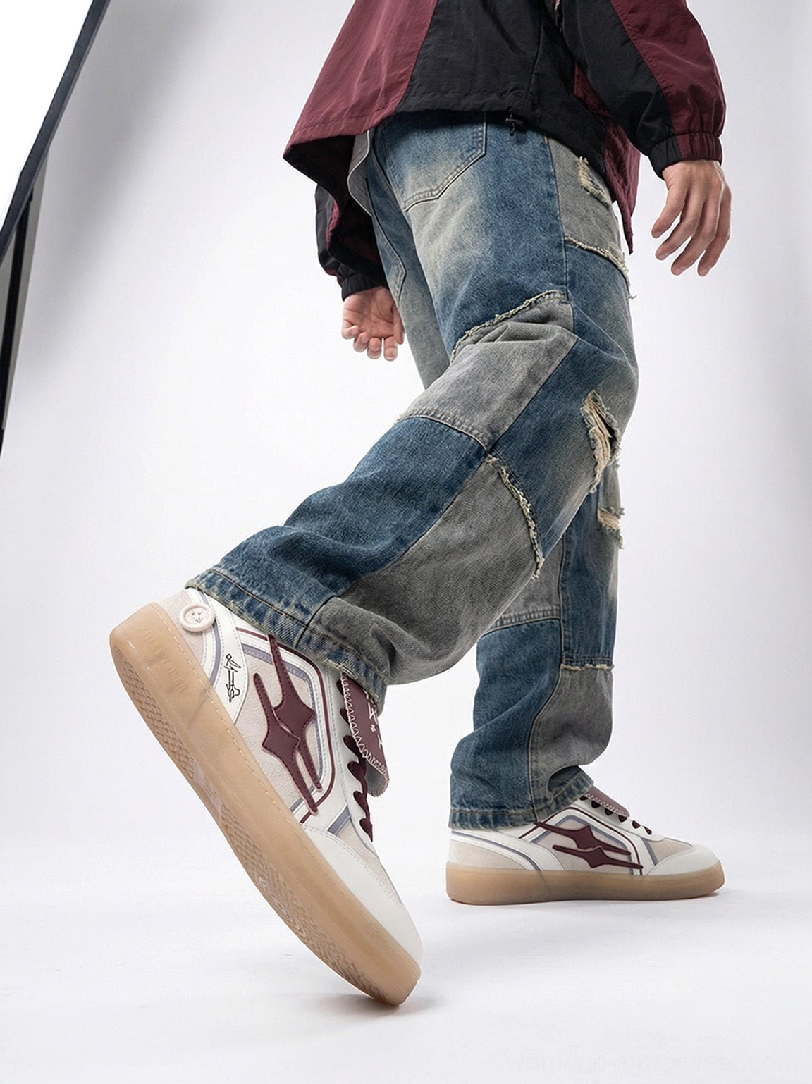 Wine red strap retro trainer sneakers shown while walking with patchwork denim and a casual windbreaker