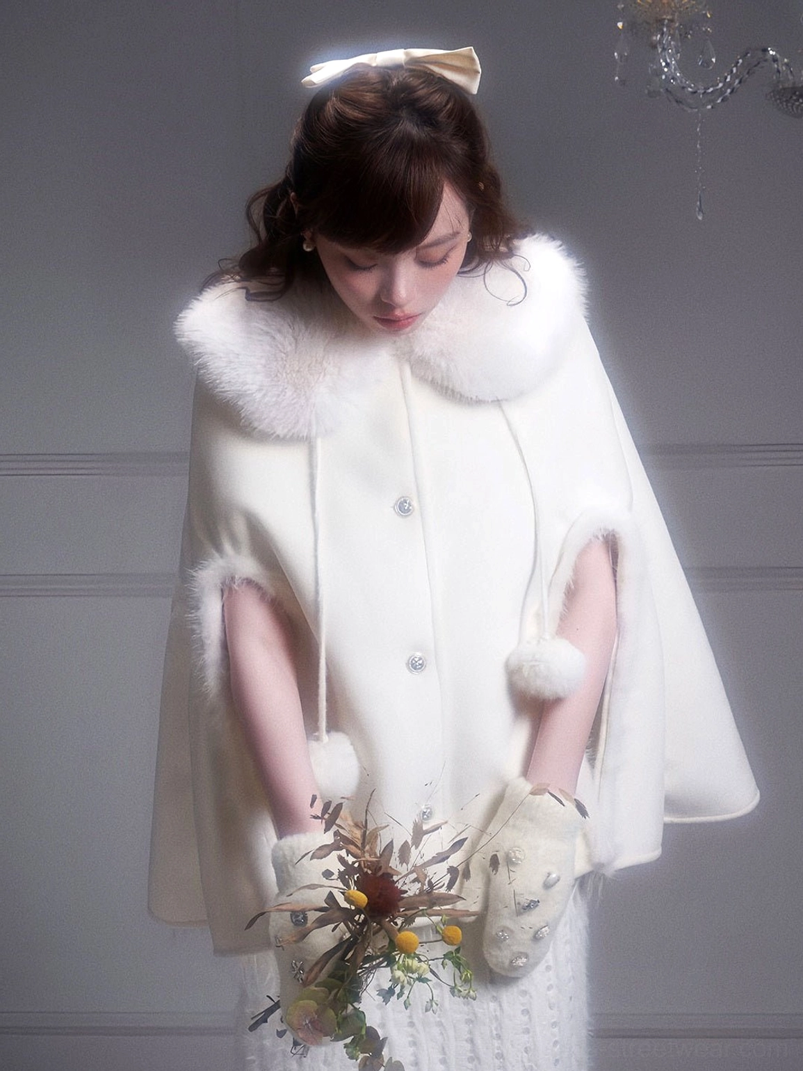 Winter white cape coat front three-quarter view featuring plush collar front buttons and pom-pom pendants