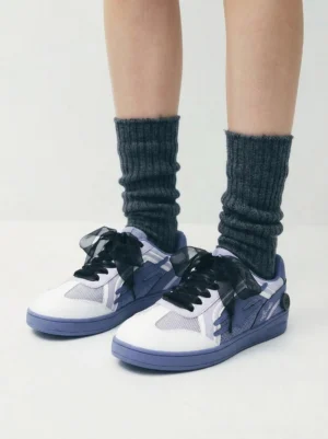 Model wearing wisteria lavender retro court sneakers with oversized black bow laces and dark gray slouch socks in a streetwear outfit