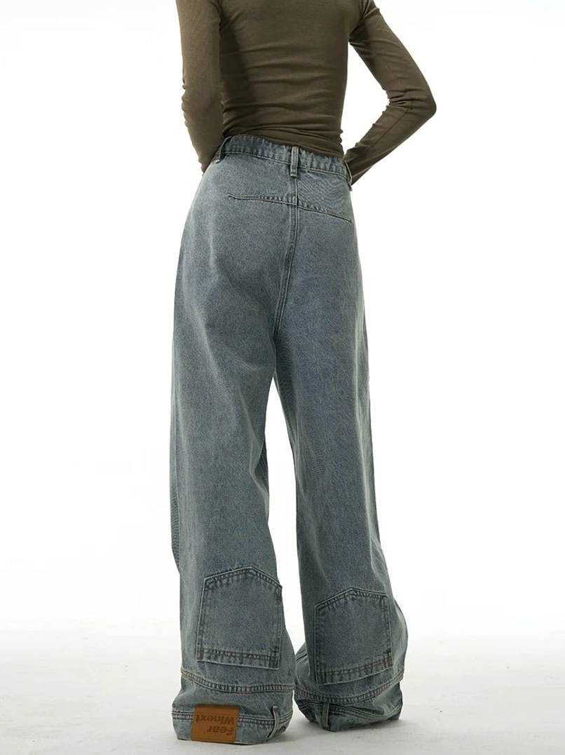Rear view of women’s faded blue wide-leg denim jeans with layered hem, lower-leg patch pockets, back waistband, and deconstructed streetwear details
