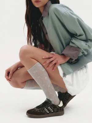 Women wearing forest leopard print low top sneakers with a mint green cropped jacket, white shorts, and patterned sheer socks in a streetwear outfit