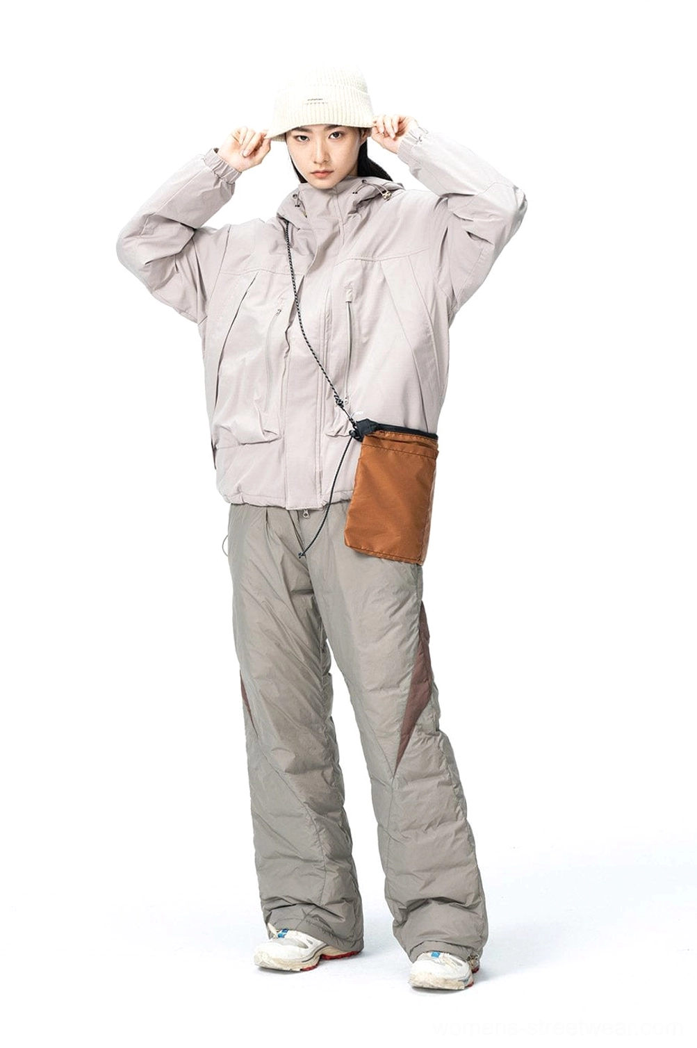 Female model wearing spliced padded track pants with a matching gray hooded jacket white beanie and brown crossbody bag