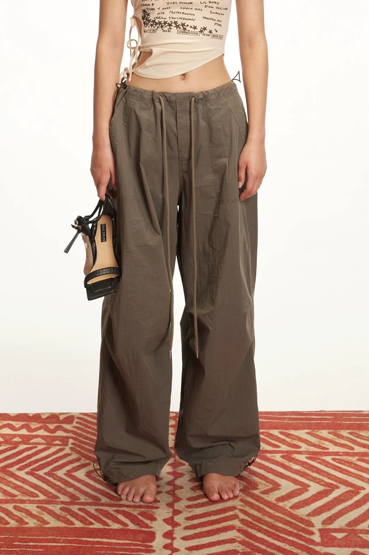 Women's dark brown drawstring parachute cargo pants with relaxed wide legs styled with a beige cropped top and handbag