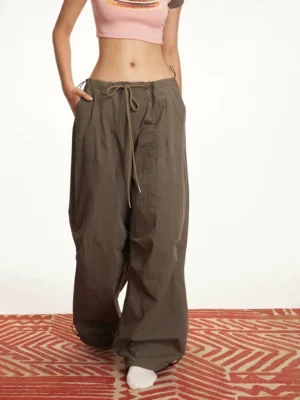 Women's dark brown adjustable hem parachute cargo pants styled with a pink cropped top in a low-angle streetwear outfit