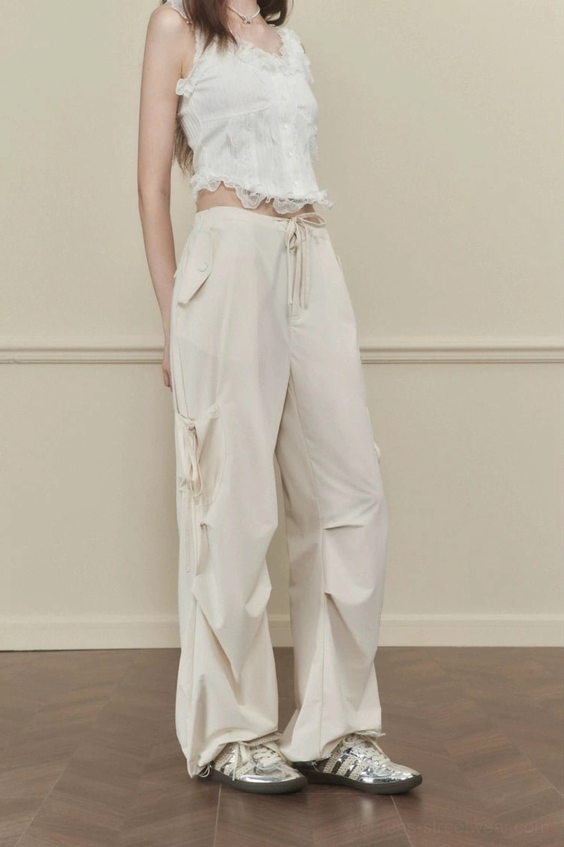 Women's apricot relaxed wide-leg cargo pants with side tie accents shown from the rear in a minimalist streetwear look