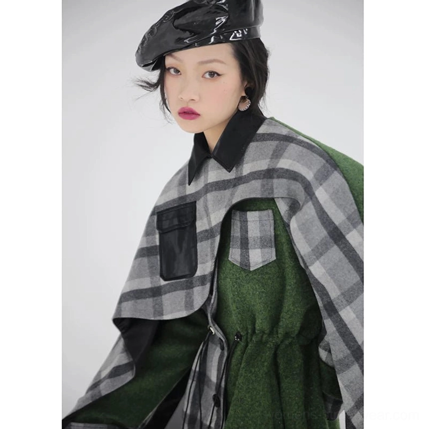 Close-up view of women's asymmetric plaid cape coat showing faux leather pocket trim, black shirt collar, adjustable drawstring waist, and layered green wool-look fabric