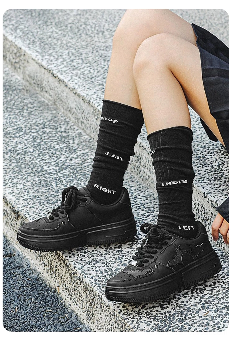 Women's black bat crest platform sneakers styled with a short skirt and black crew socks on stone steps