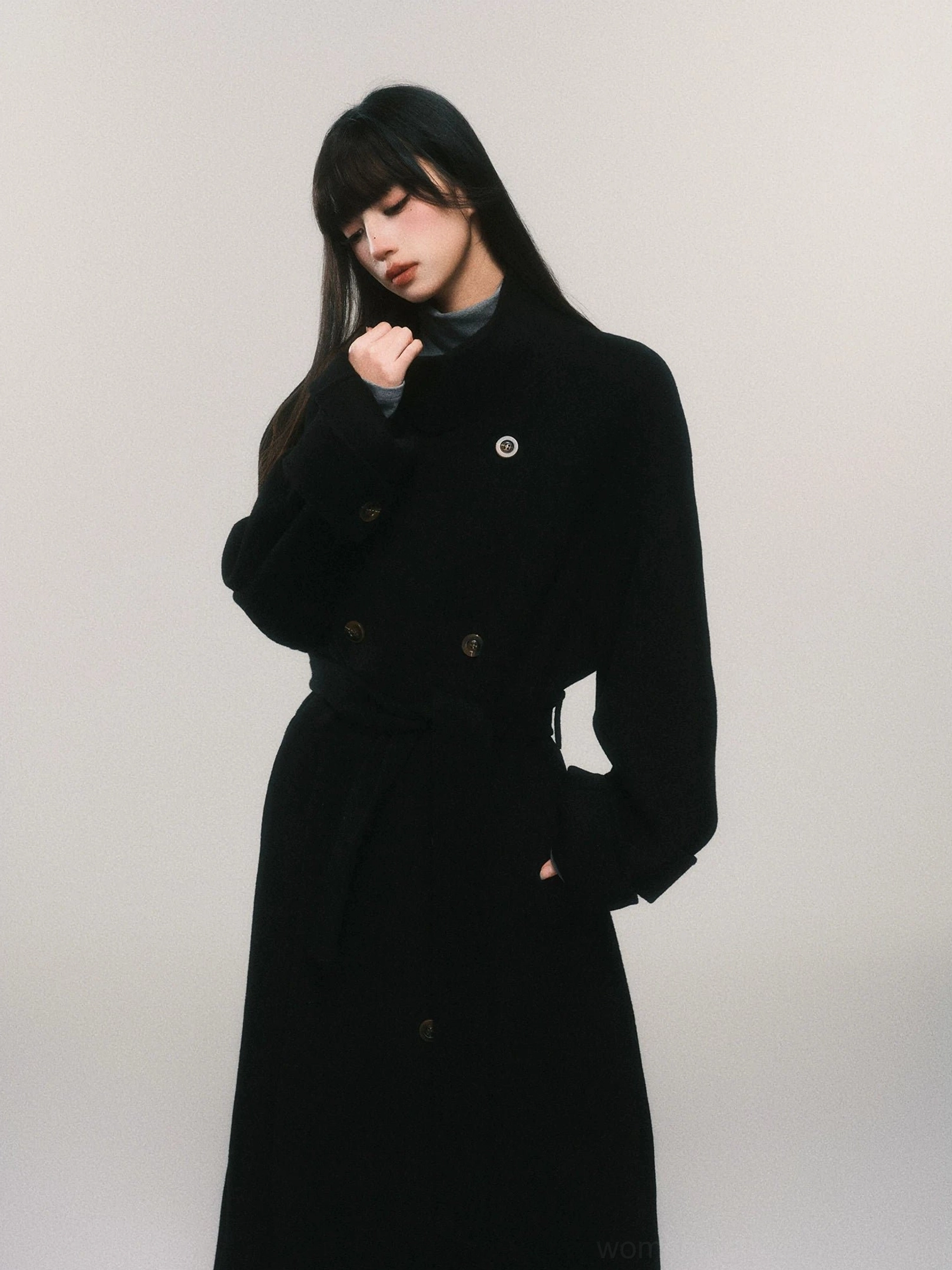 Close side view of women's black belted double-breasted wool maxi trench coat with tailored waist detail