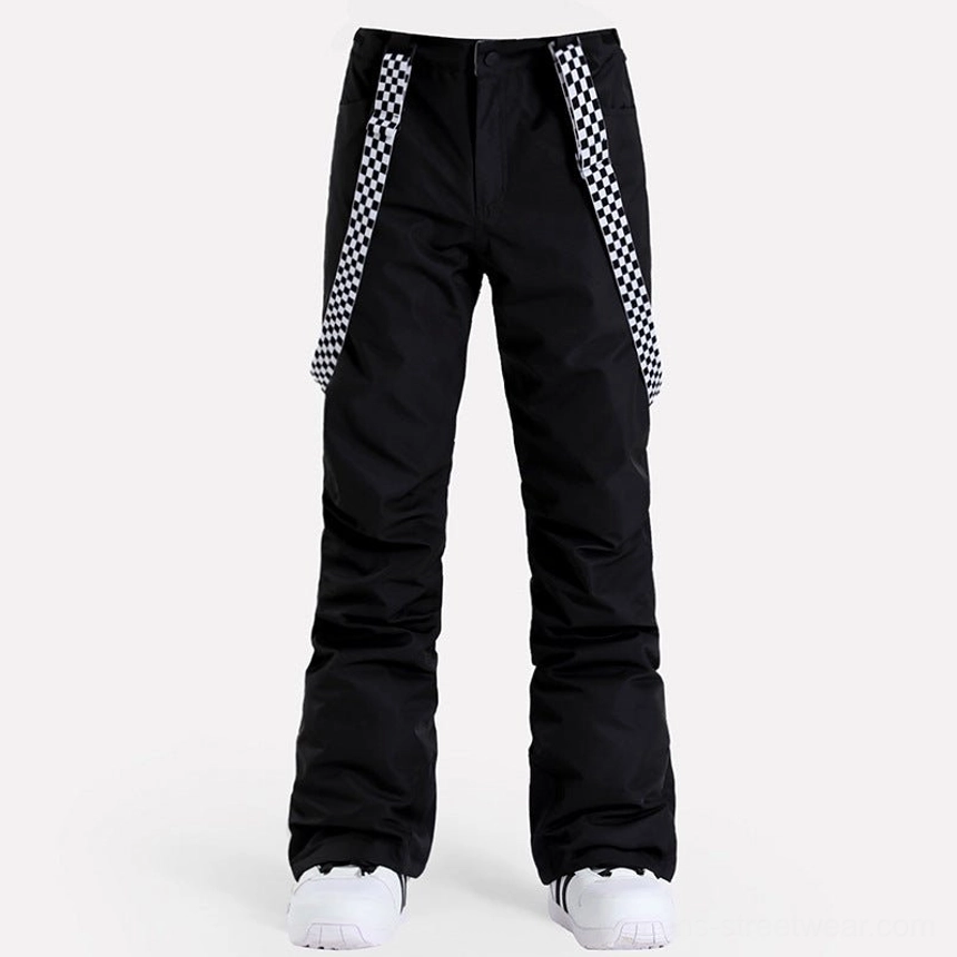 Front view of women's black checkerboard snow pants with detachable suspenders, flared ski streetwear legs, black ankle patches, and white snow shoes
