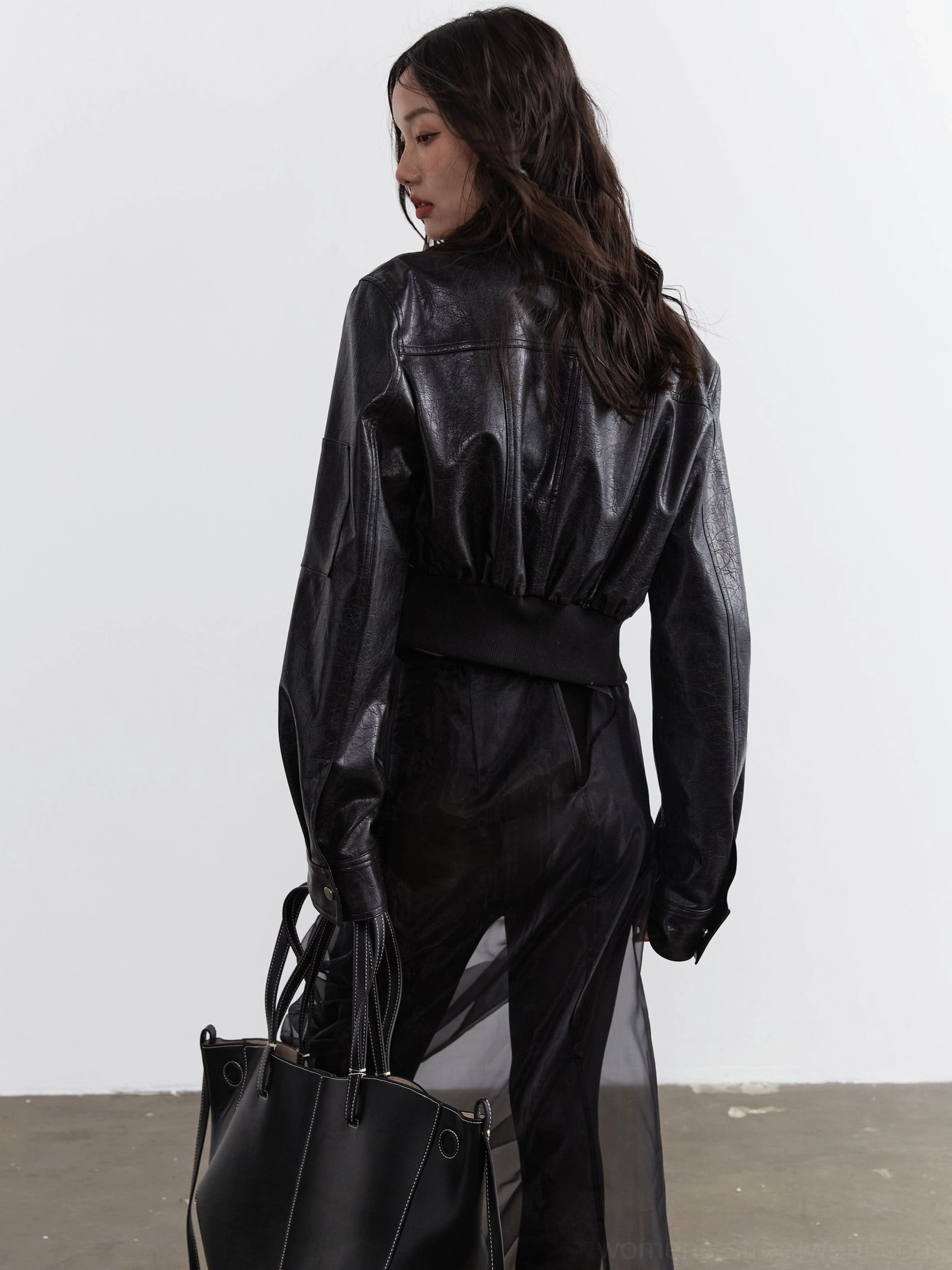 Full back view of a women's black cropped biker jacket with minimalist faux leather back, relaxed oversized sleeves, and elastic ribbed waistband
