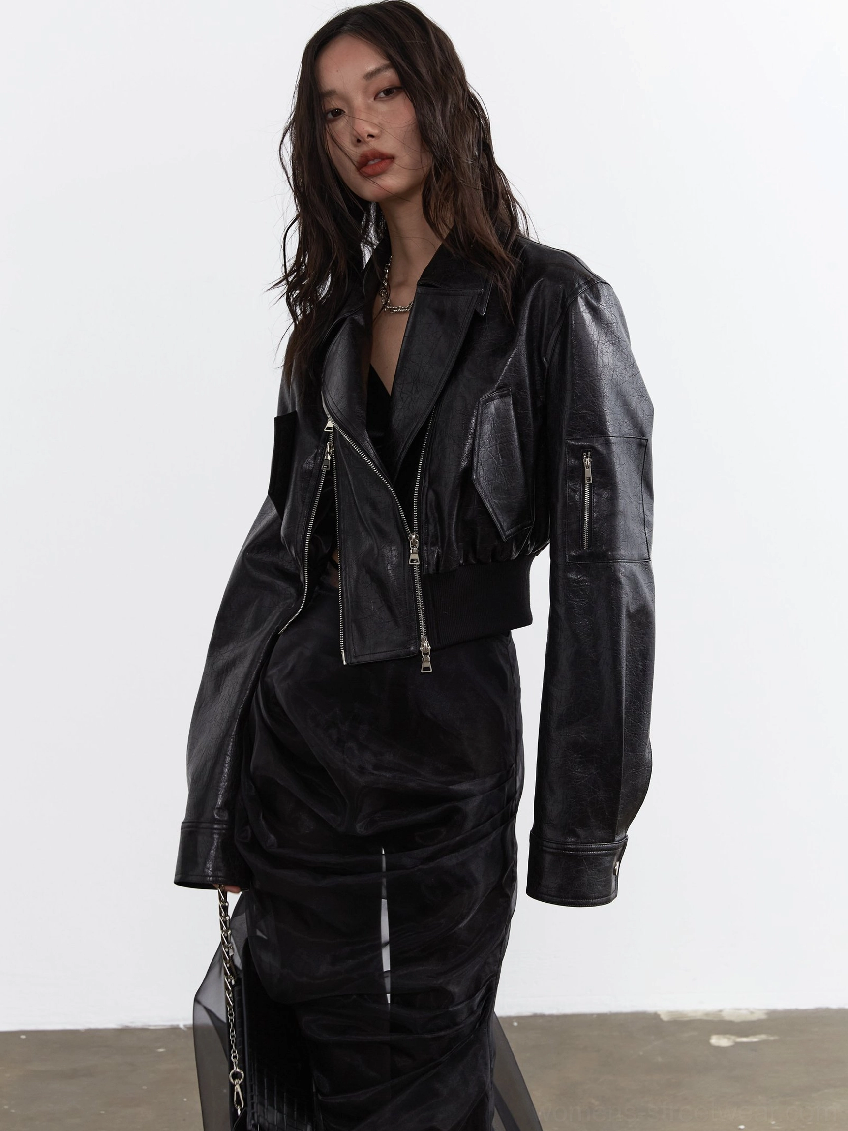 Side view of a women's black cropped faux leather biker jacket with dropped shoulders, front zip pockets, relaxed sleeves, and fitted ribbed hem