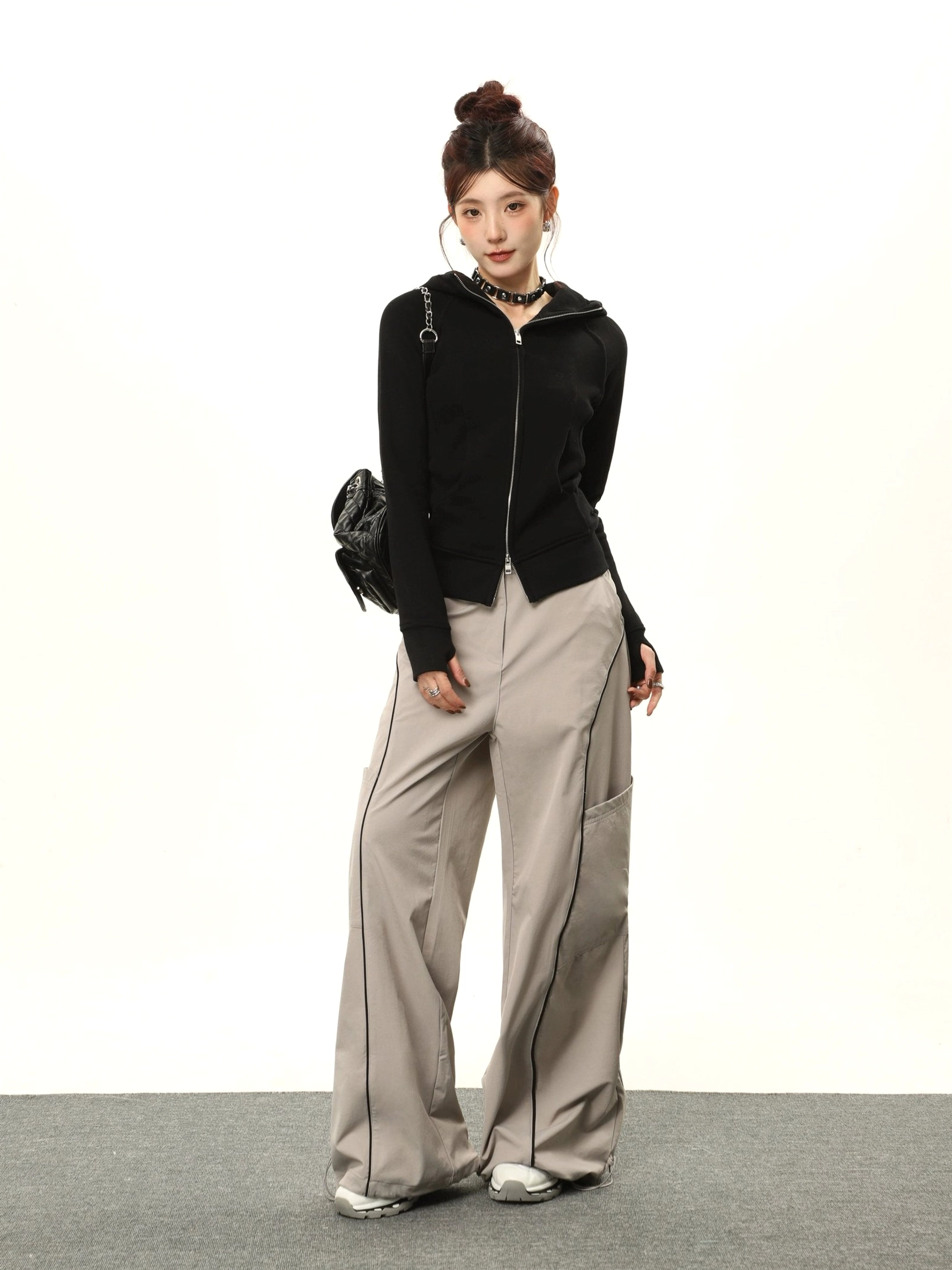 Full-body styling view of a women's black fitted zip-up hoodie worn with light gray cargo pants and a chain crossbody bag