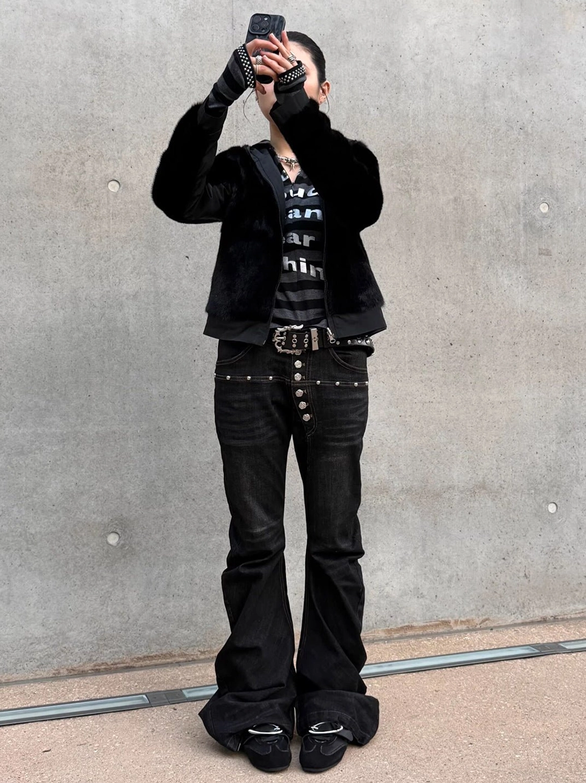 Black leather German trainer sneakers styled with a Y2K streetwear outfit, flared jeans, and statement coat