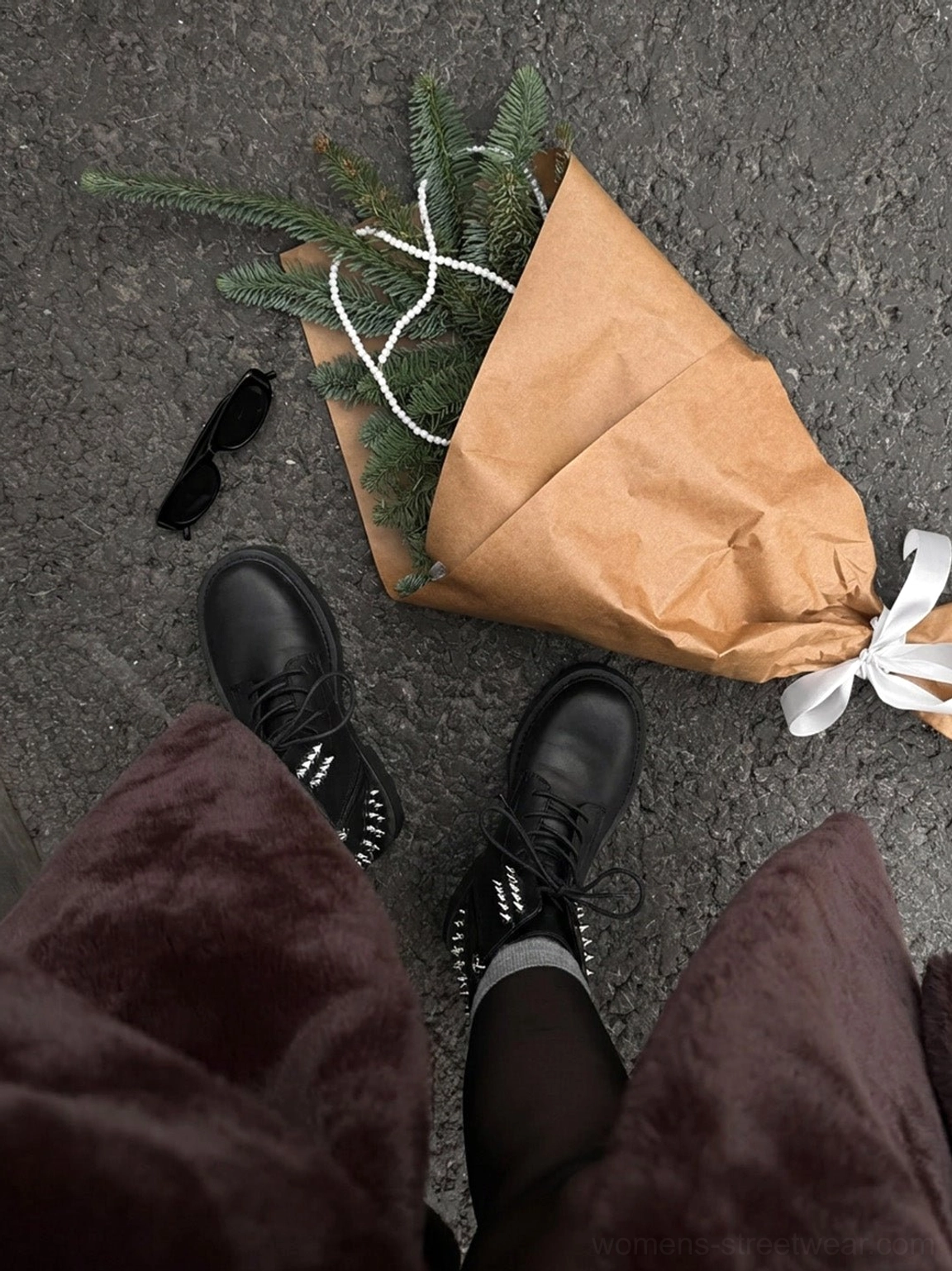 Top-down view of women's black studded leather platform combat boots worn with dark velvet trousers, bouquet, and sunglasses
