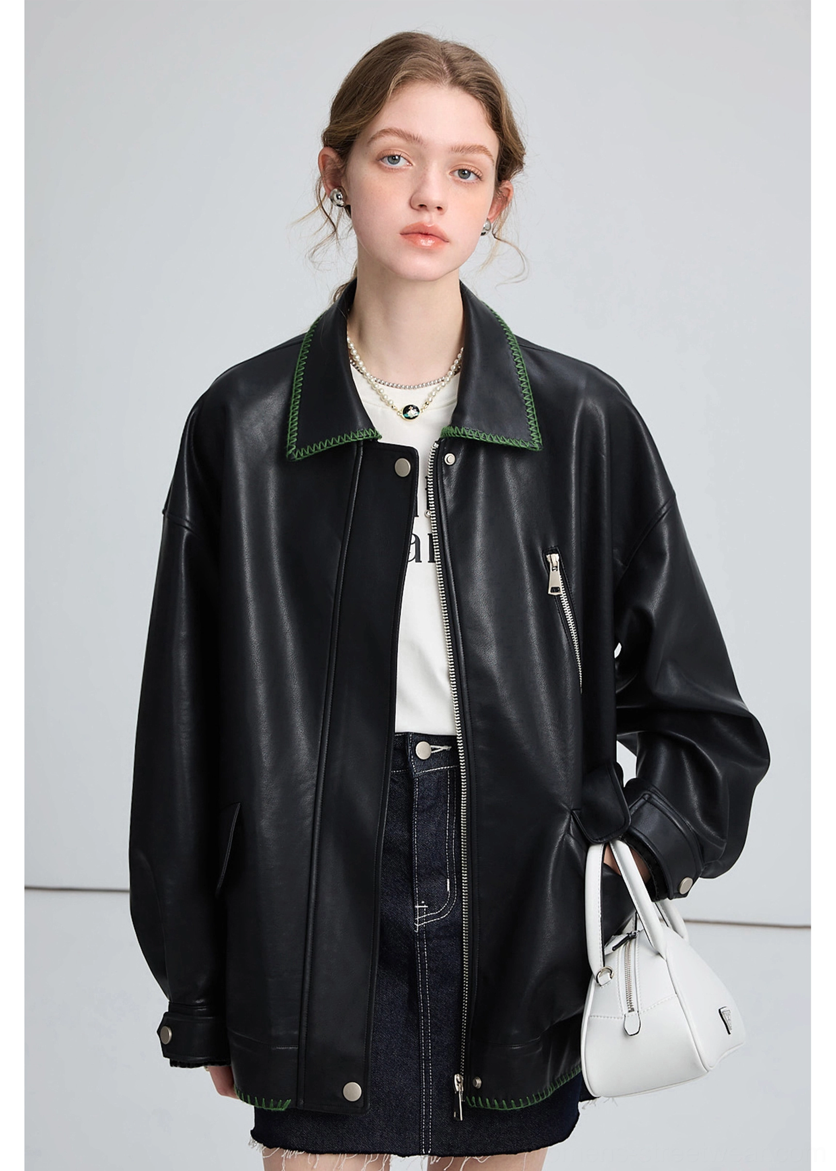 Full view of a woman wearing an oversized black PU leather biker jacket with denim skirt and white handbag