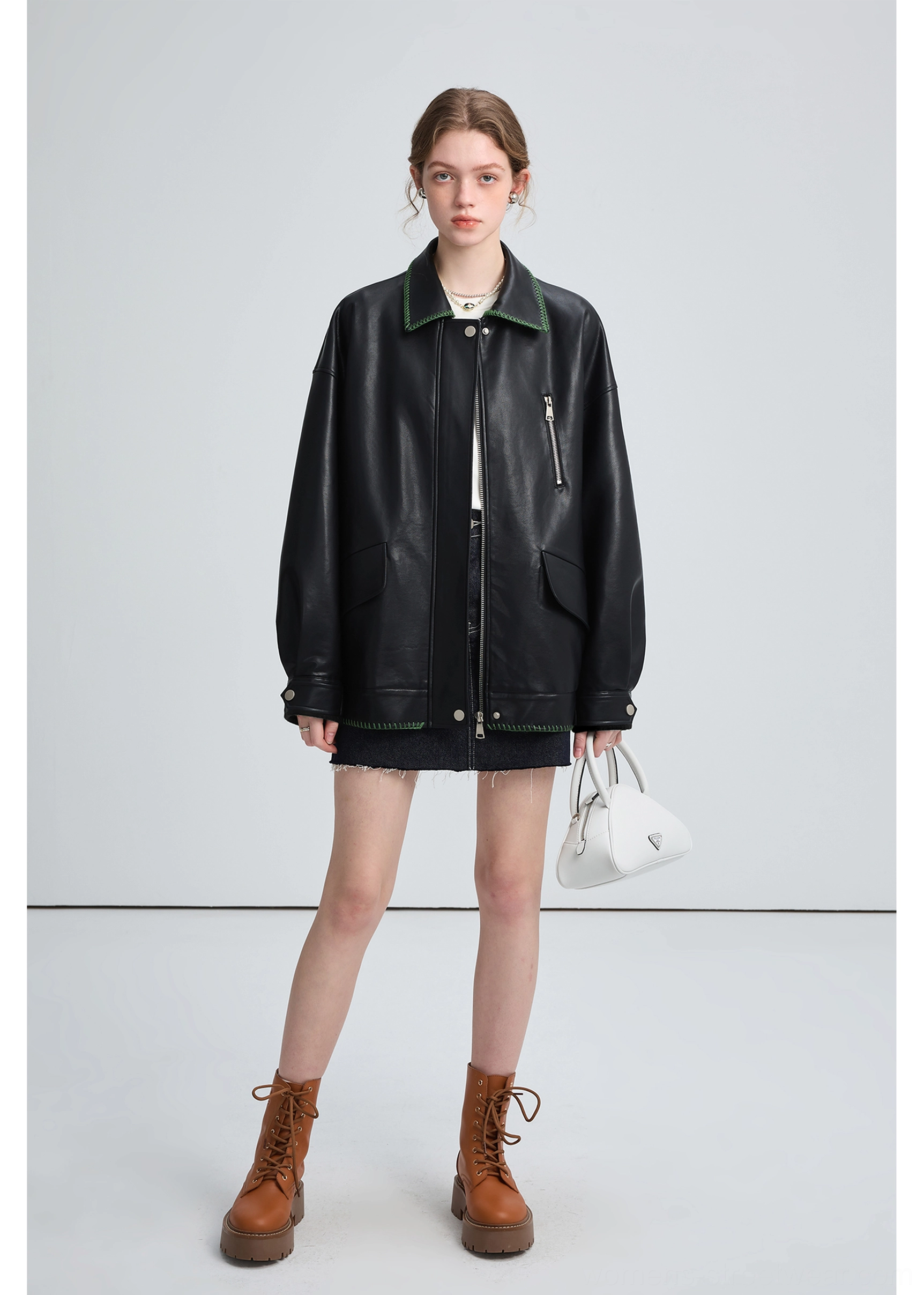 Full front streetwear styling of a woman in a black oversized PU leather biker jacket with white handbag and denim skirt