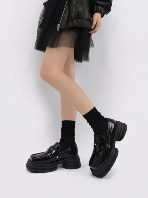 Woman wearing black chunky platform loafers with black socks leather jacket and tulle skirt in a modern streetwear outfit