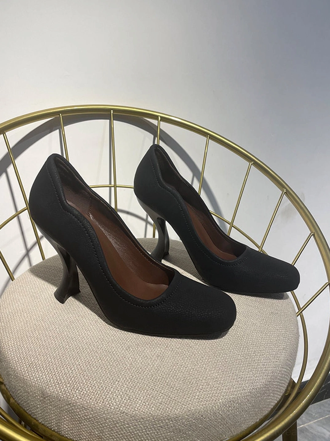 Black women's sculpted heel round-toe pumps displayed on chair showing the scalloped collar and rounded toe