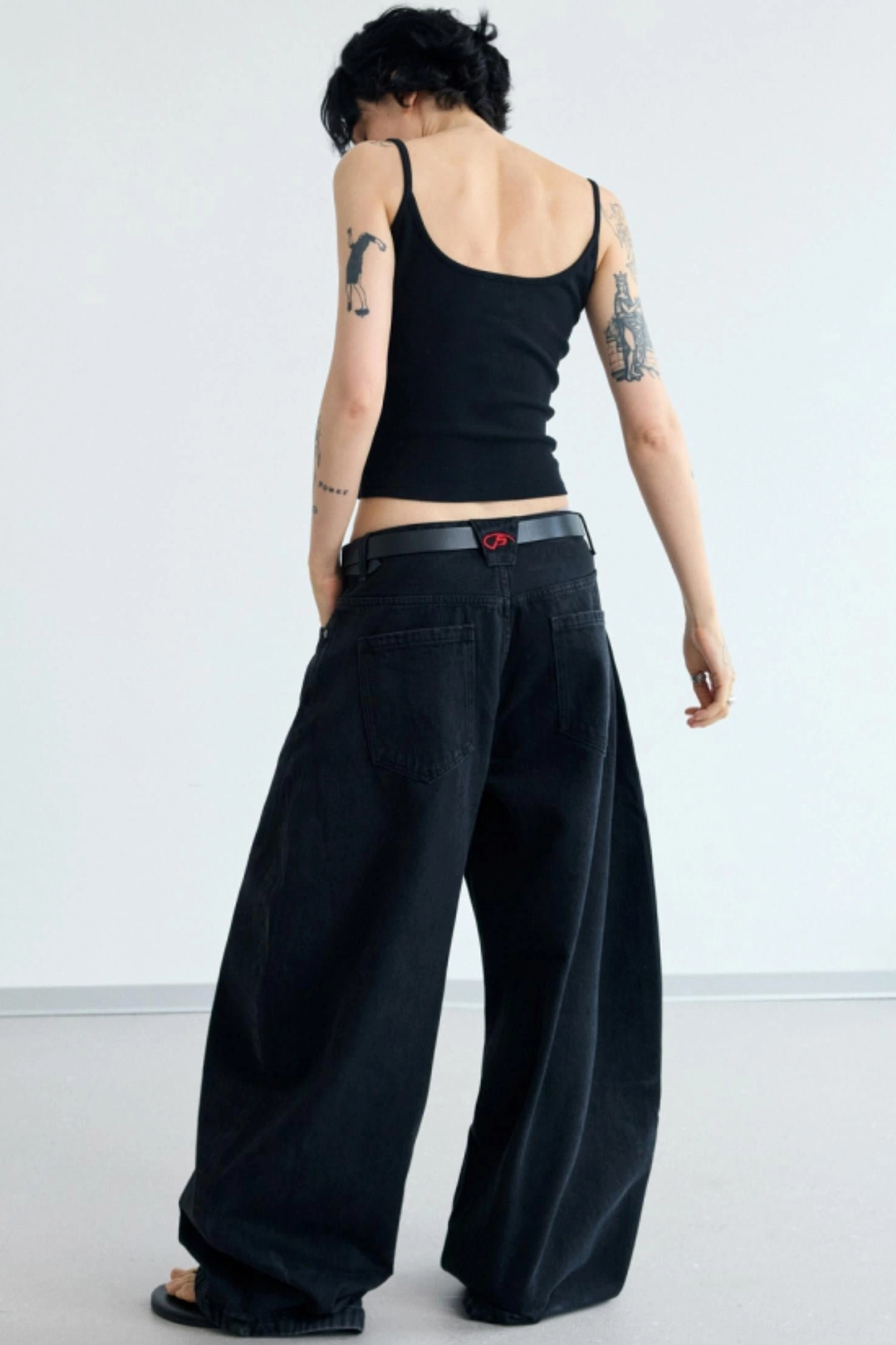 Back view of women's black slim cropped camisole tank top styled with black wide-leg streetwear jeans