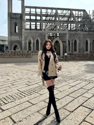 Model wearing black stretch suede over-the-knee stiletto boots with a tailored outfit in an urban Gothic brick setting