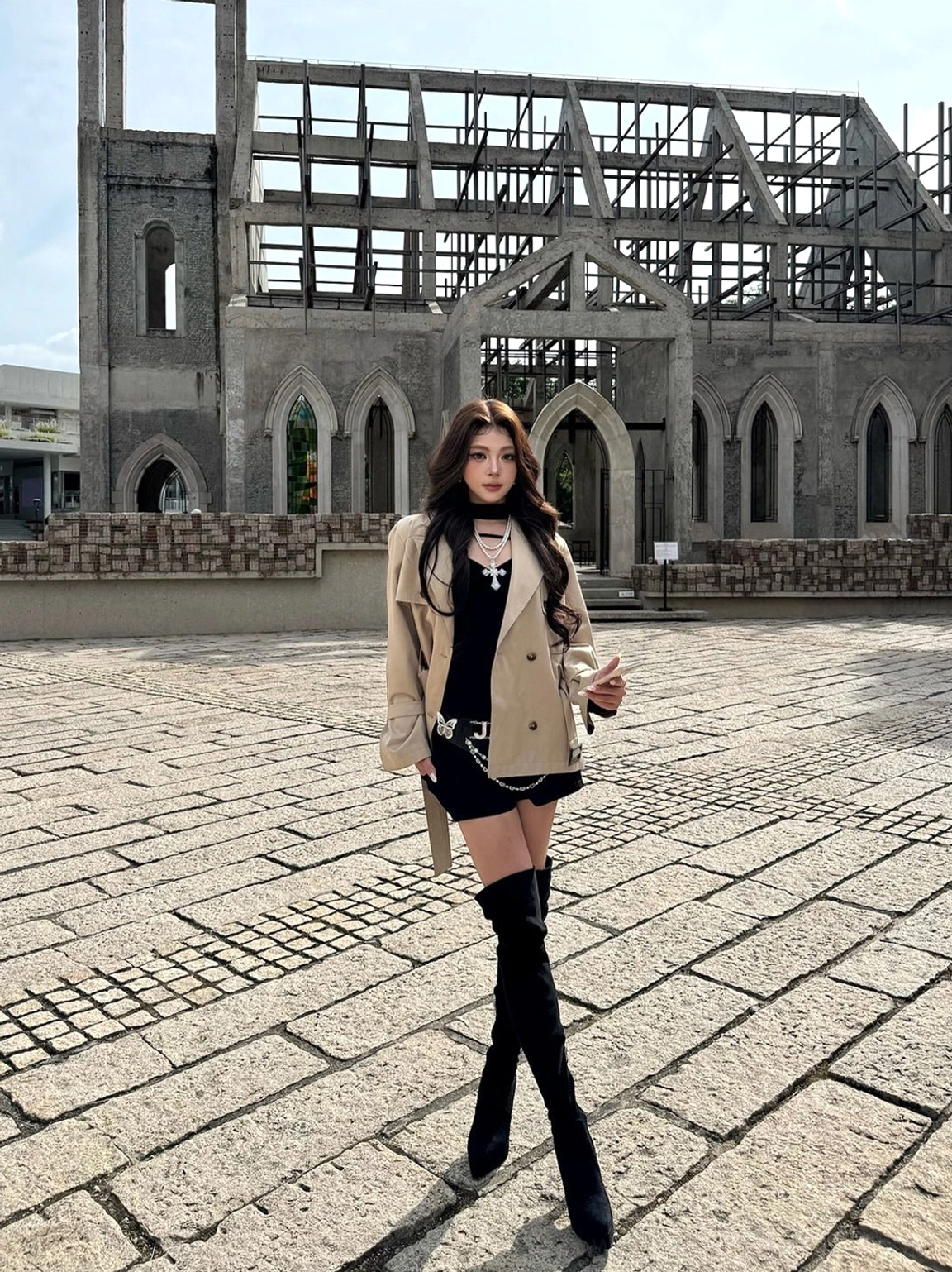 Model wearing black stretch suede over-the-knee stiletto boots with a tailored outfit in an urban Gothic brick setting