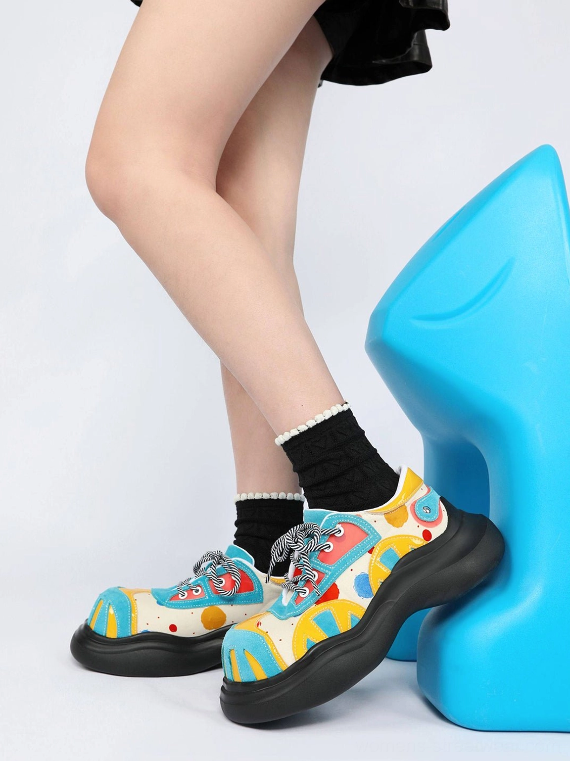 Women’s blue graffiti platform derby shoes with abstract primary-color print styled beside a bright blue stool