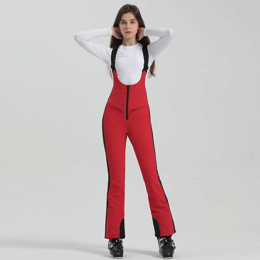 Women's bright red bib ski overalls with black suspender straps, black side panels, front zipper, flared legs, and ski boots
