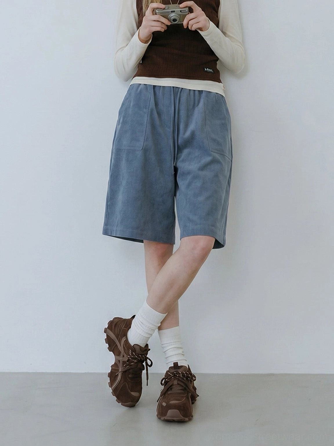Side on-foot view of women's brown cross-strap chunky trail runner sneakers styled with white socks and casual shorts
