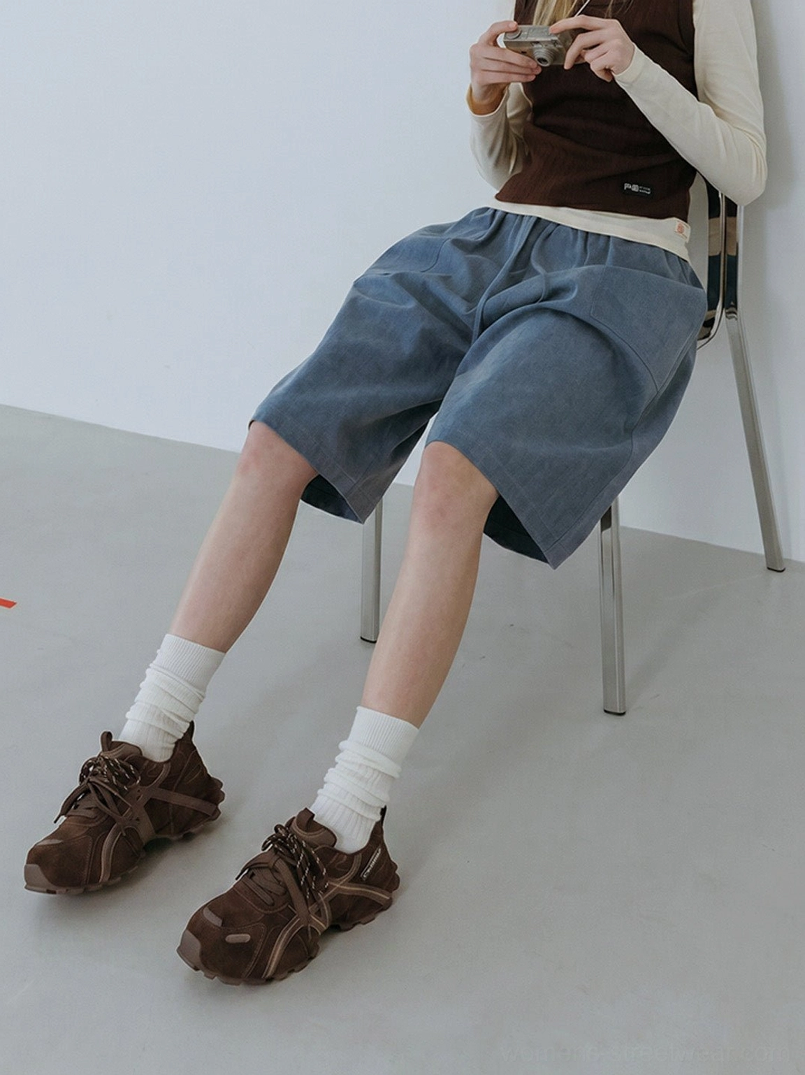 Female model sitting in women's brown cross-strap chunky trail runner sneakers showing cushioned gorpcore-inspired styling