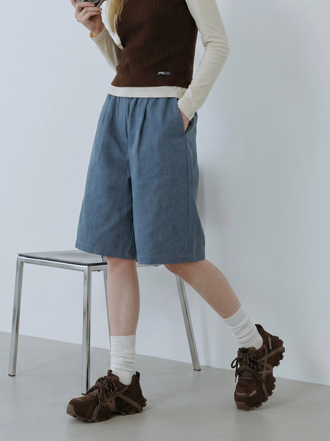 Women's brown cross-strap chunky trail runner sneakers worn with relaxed neutral streetwear outfit in studio setting
