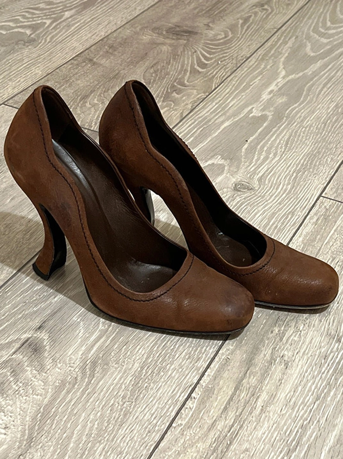 Brown women's sculpted heel round-toe pumps in front three-quarter view showing scalloped asymmetric topline and contrast stitching