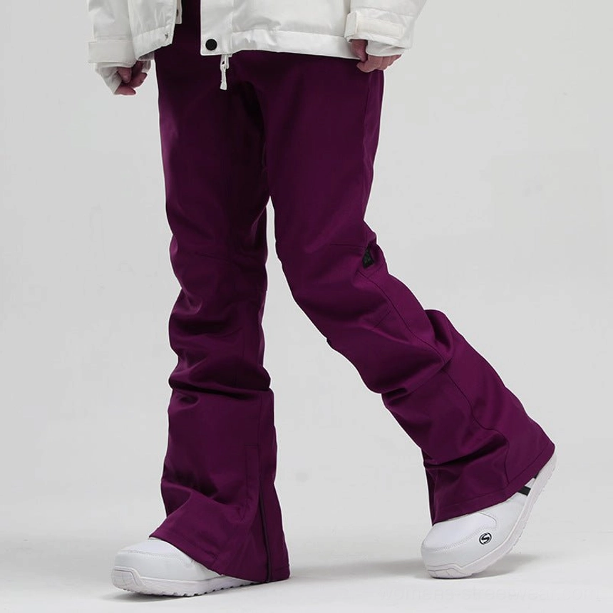 Burgundy women's flared snowboard pants with subtle outer thigh detail, adjustable boot hem zipper, white ski boots, and winter jacket