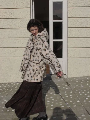 Women's cream floral print sherpa hooded jacket with black contrast piping shown from the rear outdoors