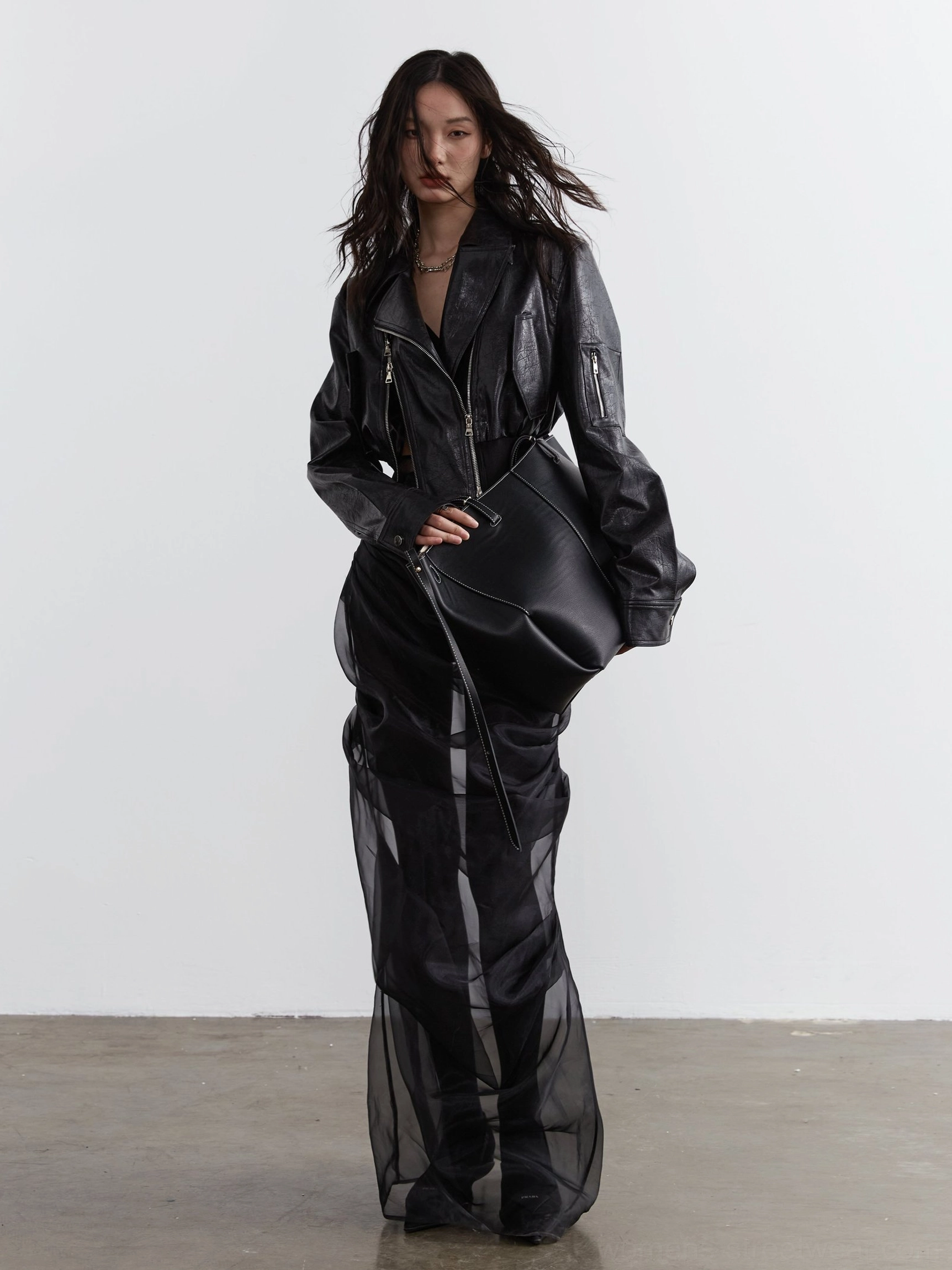 Front full view of a women's cropped black biker jacket with tailored length, silver zipper hardware, faux leather finish, and all-black monochrome outfit styling
