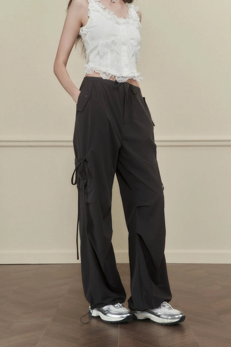 Women's dark gray high-waisted side-tie cargo pants with wide legs and utility pocket details styled with silver sneakers