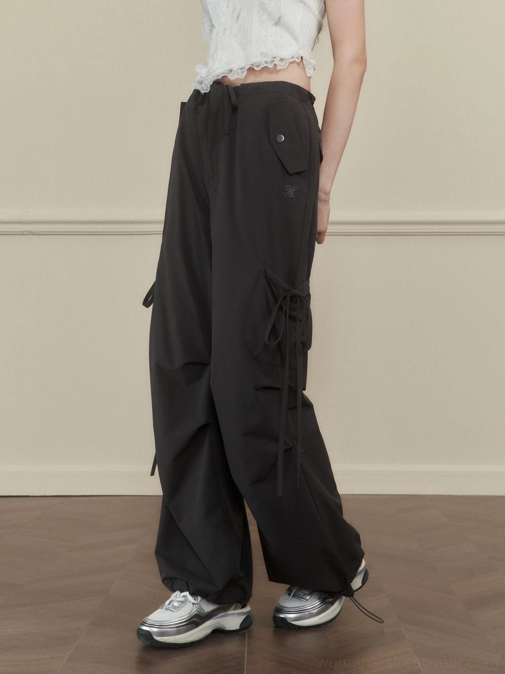 Women's dark gray side-tie wide-leg cargo pants shown from a low rear three-quarter view in a streetwear studio outfit